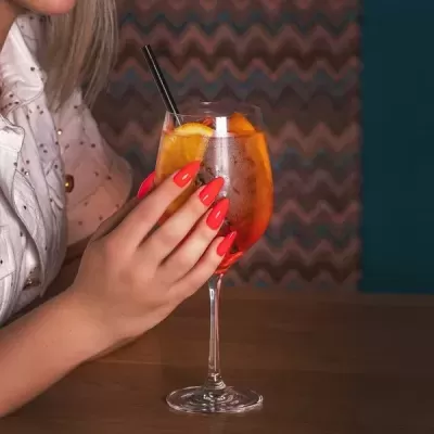 Bebida em copo com fatia de laranja e mão com unhas vermelhas