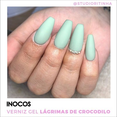 Mão com unhas de gel verde fosco e pequenas pedras brilhantes na unha do anelar