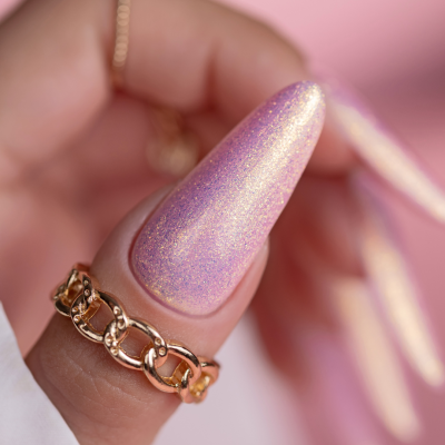 Unha artificial rosa cintilante com anel dourado em fundo rosa