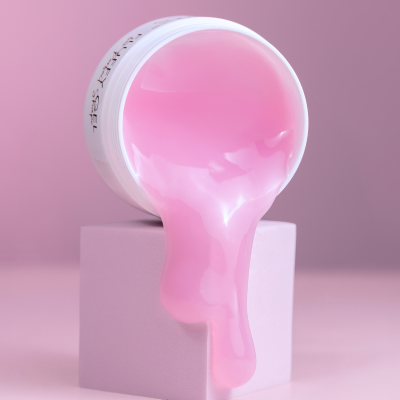 Recipiente branco aberto com creme rosa a escorrer sobre cubo rosa, fundo rosa