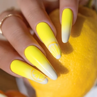 Unhas decoradas em amarelo e branco com desenhos de limão, segurando limão amarelo