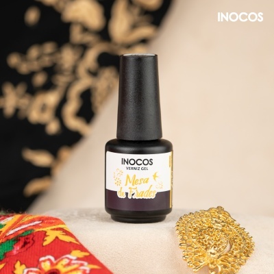 Frasco de verniz gel preto INOCOS sobre superfície clara com tecido colorido e peça dourada ao lado.