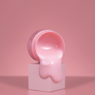 Frasco rosa com líquido rosa escorrendo sobre cubo branco em fundo rosa