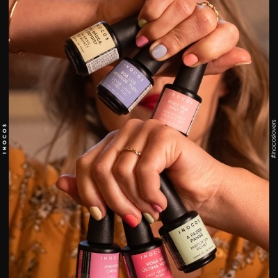 Frascos de verniz gel INOCOS em várias cores segurados por mãos femininas com unhas coloridas