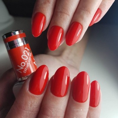 Unhas pintadas de vermelho vivo segurando frasco de verniz