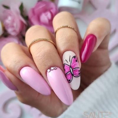 Unhas decoradas rosa com borboleta pintada e strass, anéis dourados, fundo com flores e cosméticos