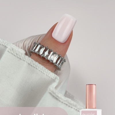 Unha com verniz gel rosa claro e anel prateado em fundo cinzento claro