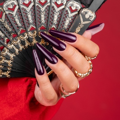 Mão feminina com unhas roxas brilhantes segurando um leque preto decorado.