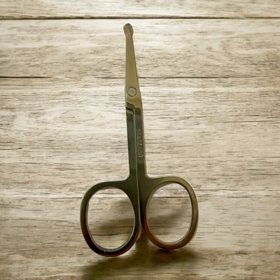 Tesoura pequena de metal prateado com pontas arredondadas sobre madeira clara