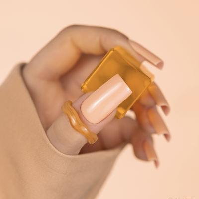 Mão feminina com unhas compridas castanho claro segurando peça quadrada de plástico laranja translúcido e anel laranja ondulado