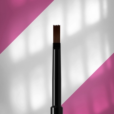 Pincel de maquilhagem com cabo preto e cerdas castanhas sobre fundo branco e rosa