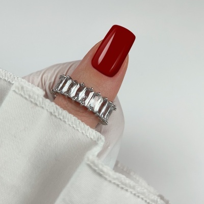 Anel prateado com pedras transparentes no dedo polegar com unha vermelha escura