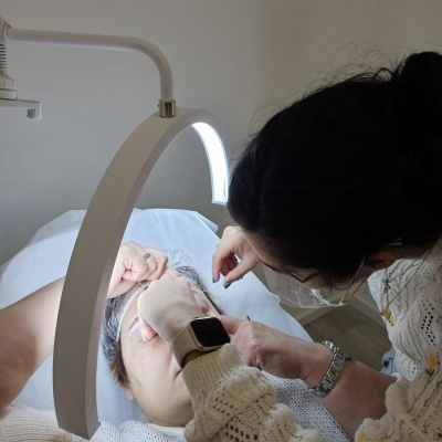 Pessoa a receber tratamento facial de outra sob luz circular branca