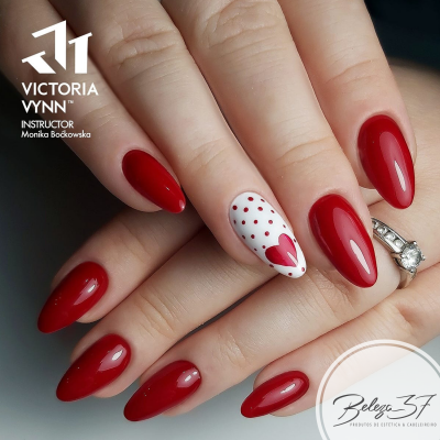 Unhas almendradas vermelhas com uma unha branca decorada com pontos e coração vermelho