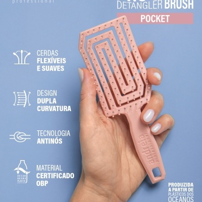 Escova de cabelo rosa claro com cerdas flexíveis e design curvo sendo segurada por uma mão sobre fundo azul