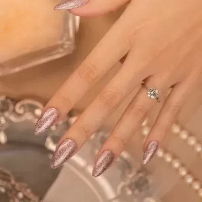 Mão com unhas rosa metálico e anel de diamante
