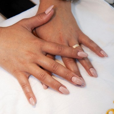 Mãos femininas com unhas artificiais nude brilhante e anel dourado