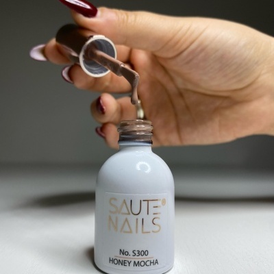 Frasco de verniz de unhas Saute Nails Honey Mocha aberto com pincel a aplicar o verniz
