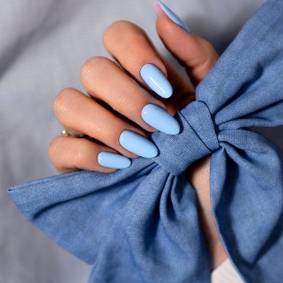 Unhas pintadas de azul claro segurando laço azul de tecido.