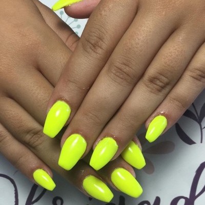 Mãos com unhas amarelo neon vibrante sobre superfície branca com texto roxo.
