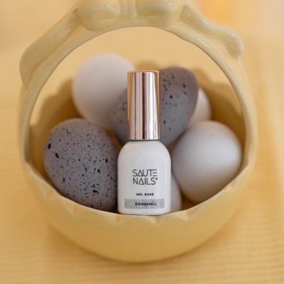Frasco de verniz branco em cesto amarelo com ovos brancos e cinzentos com manchas.