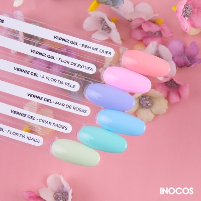 Amostras de verniz gel em várias cores pastel com etiquetas de nomes em português sobre fundo rosa com flores