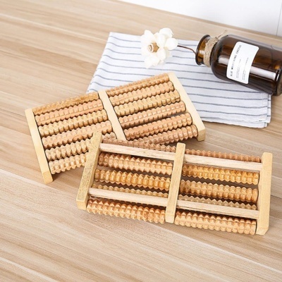 Rolos de madeira para massagem dos pés numa mesa com pano listrado e frasco de vidro com flor.