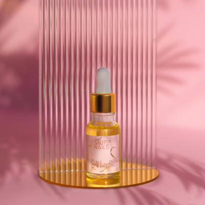 Frasco de óleo para unhas com conta-gotas em fundo rosa e base dourada