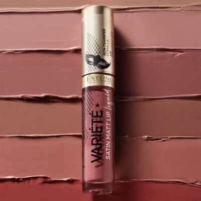 Batom líquido mate com embalagem transparente e tampa dourada sobre fundo texturizado em tons rosa e castanho.