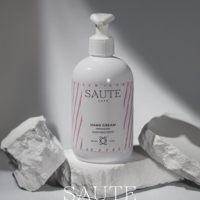 Frasco branco de creme de mãos SAUTE CARE com rótulo branco e rosa sobre pedras brancas