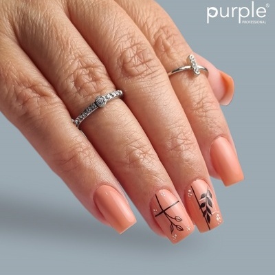 Mão feminina com unhas postiças cor pêssego e desenhos pretos e brancos, dois anéis prateados, fundo cinza