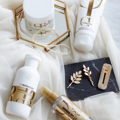 Produtos OI Reflections em embalagens brancas com detalhes dourados sobre tecido branco e acessórios dourados