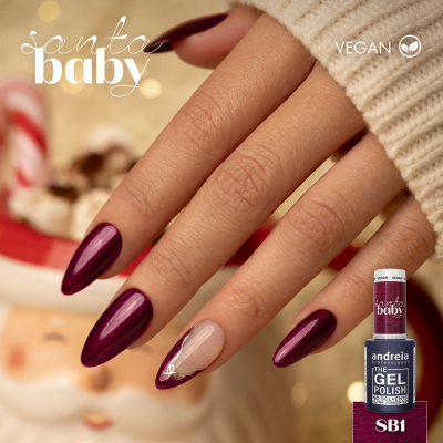 Mãos com unhas de verniz gel vinho escuro e uma decoração dourada, perto de frasco de verniz e decoração natalícia.