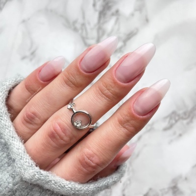 Mãos femininas com unhas compridas nude translúcido e anel prateado com pedra