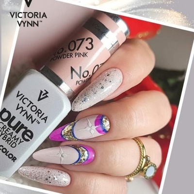Unhas decoradas com verniz rosa, roxo e dourado, e frascos de verniz Victoria Vynn ao fundo