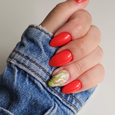 Unha vermelha com unha decorativa creme e verde, mão com manga de casaco de ganga azul