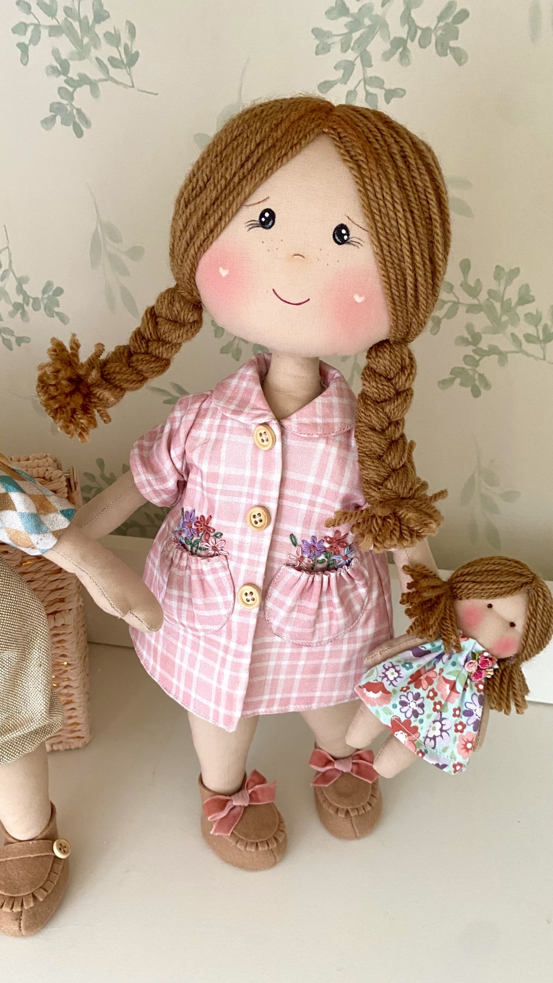 Aula online boneca Constança Boneca de pano com casaco rosa xadrez segurando boneca pequena vestida de floral