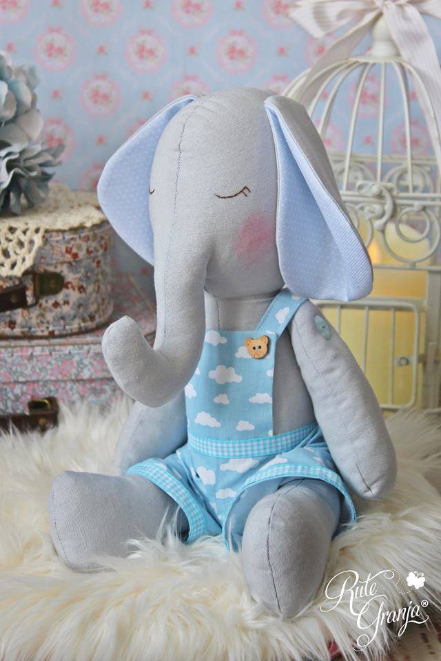 Kit Elefante Sebastião Pelúcia de elefante cinzento com roupa azul às nuvens e botões de urso sentado