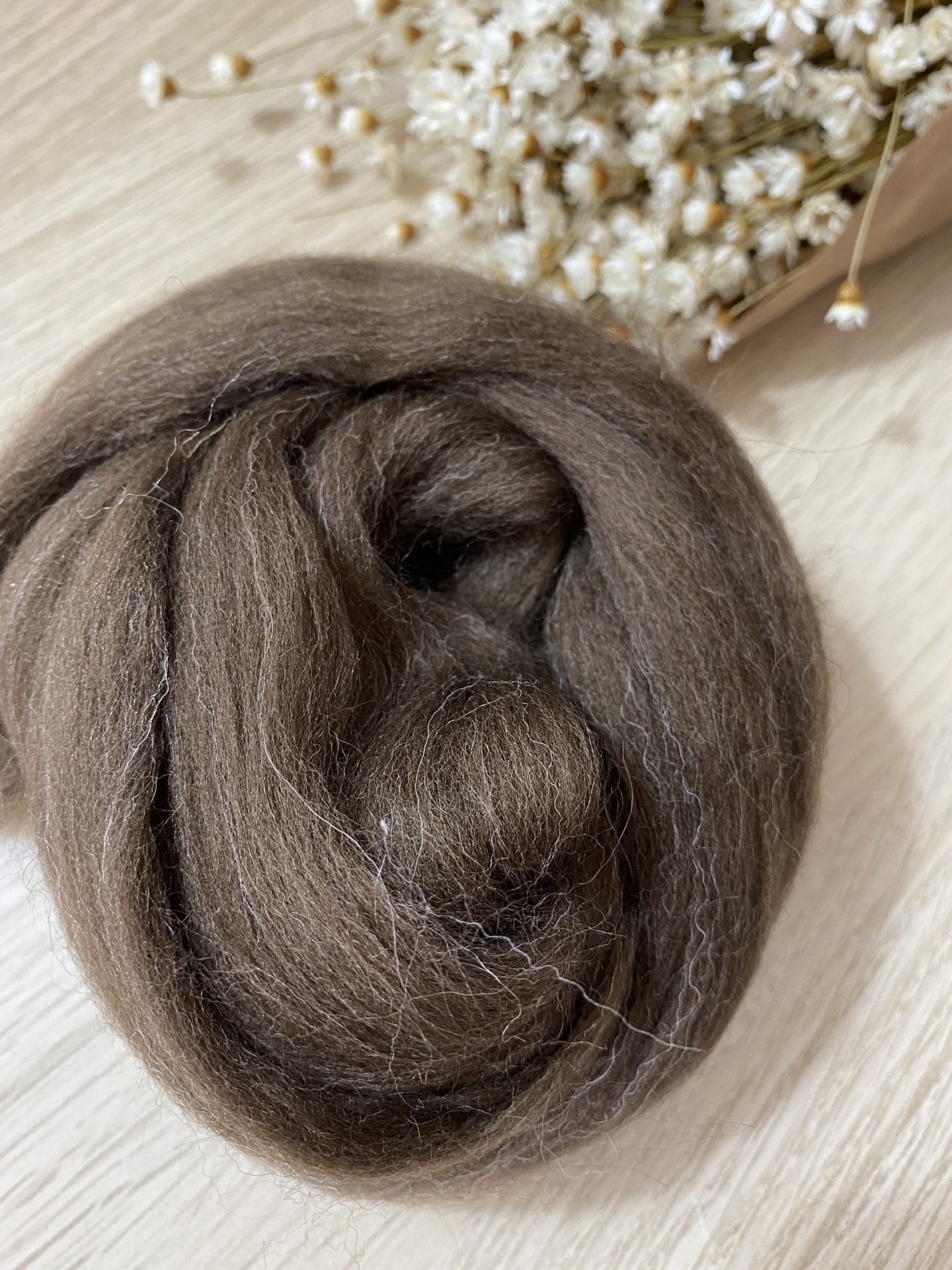 Lã feltrada castanha (1metro) Lã cardada castanha enrolada com flores brancas ao fundo