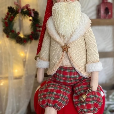 Boneco decorativo de Natal com barba, casaco bege, calças xadrez e chapéu vermelho sentado