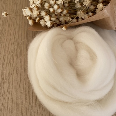 Rolo de lã branca com ramo de flores secas em papel castanho sobre madeira clara