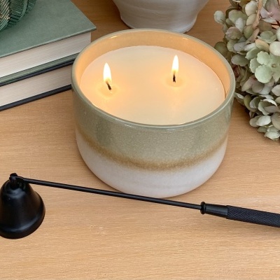 Vela decorativa acesa numa base cerâmica verde e branca, com isqueiro longo e livros ao lado