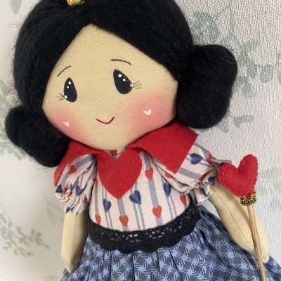 Boneca de pano vestida com padrão de corações e saia azul segurando varinha com coração