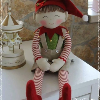 Boneco decorativo de tecido sentado numa mesa branca com gorro vermelho e roupa colorida