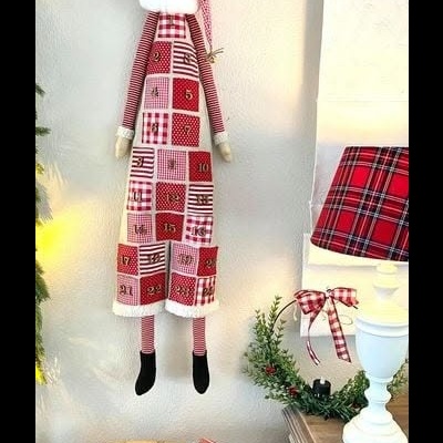 Boneco de Natal com roupa numerada e riscas em tons de vermelho e branco pendurado na parede