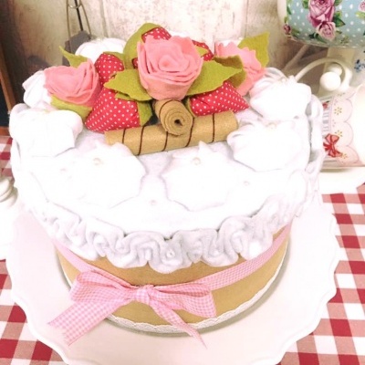 Bolo decorativo com flores de tecido e laço rosa sobre toalha xadrez