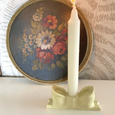 Porta-vela em forma de laço com vela branca acesa diante de prato floral
