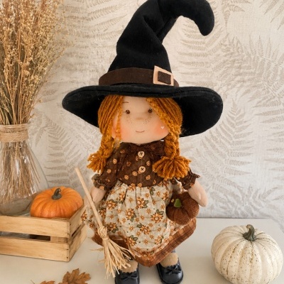 Boneca de pano de bruxa com chapéu preto e vestido floral com decoração de abóboras e folhas secas