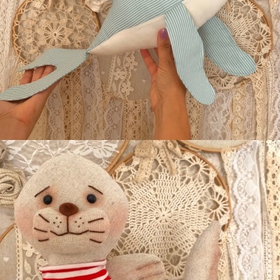 Duas peluches de golfinho azul às riscas e foca bege com roupa às riscas vermelhas e brancas, com bordados florais