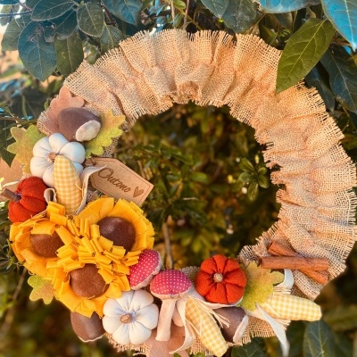 Coroa decorativa em tecido com flores, cogumelos e abóboras, com etiqueta 'Outono'